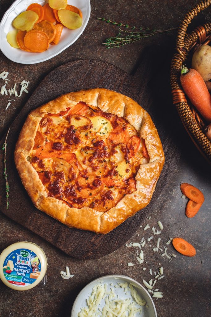 Tartă rustică tip galette cu rondele de morcov și cartof dulce, rumenită la cuptor, pe un fundal închis.