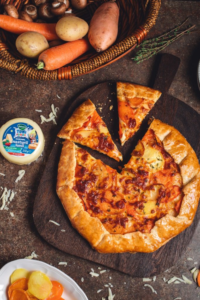 O felie de tartă sărată cu legume și crustă de cașcaval, servită pe un tocător de lemn, rețetă potrivită pentru copii.